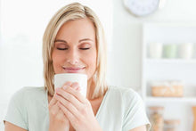 Load image into Gallery viewer, Smiling woman with eyes closed enjoying La Colombe Honduras Decaf coffee